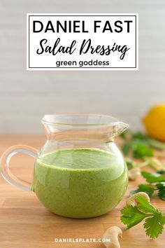 a green smoothie in a glass pitcher on a wooden table with parsley next to it