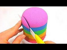 a person is holding a yellow handled scissors next to a colorful cup that has been made out of sponges