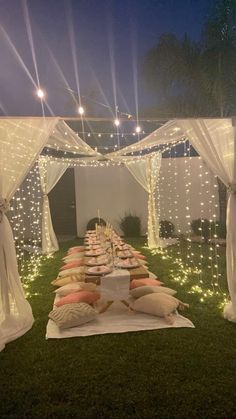 a long table covered with pillows and lights in the middle of an outdoor area at night