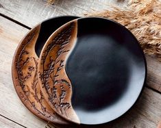 two black and brown plates sitting on top of a wooden table next to some dry grass