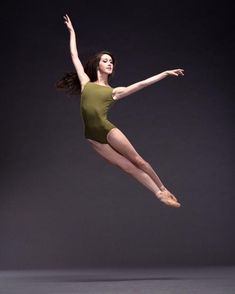 a woman in a green leotard is doing a ballet move with her legs spread out