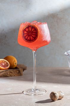 a wine glass filled with pink liquid and garnished with grapefruits