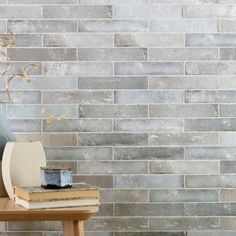 a table with books and vase on top of it next to a gray brick wall