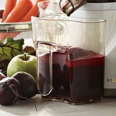 a blender filled with liquid sitting on top of a counter next to fruits and vegetables