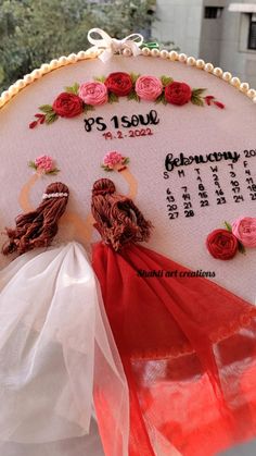 a hand embroidered wedding date sign with red ribbon and flowers on it, in front of a building