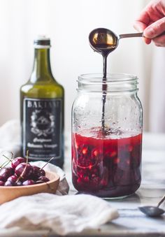 a person pouring liquid into a jar filled with cherries