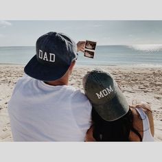 a man and woman sitting on the beach with their arms around each other looking out at the ocean