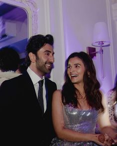 a man and woman standing next to each other in front of a purple lit room