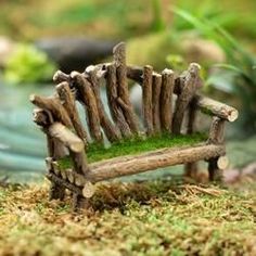 a miniature wooden bench made out of sticks and moss sitting on the ground in front of a pond