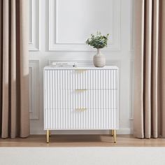 a white chest of drawers with a plant on top and curtains in the corner behind it