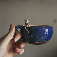 a hand holding a blue ceramic cup with a small mouse on it's side