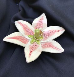 a white and pink flower brooch sitting on top of a black cloth