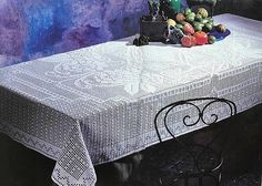 the table cloth is white and has an intricate design on it, along with fruit