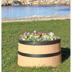 a wooden barrel filled with flowers sitting on top of a lush green field next to a lake