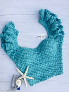 a blue knitted hat with ruffles and starfish on the side next to it