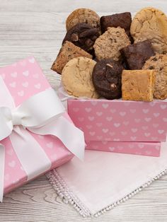 a pink box filled with cookies next to a white and pink gift bag on top of a wooden table