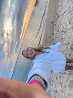 a woman standing on top of a sandy beach next to the ocean with her leg in the air