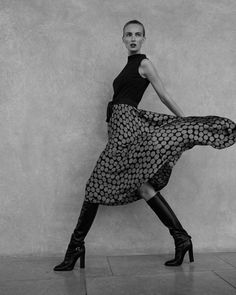 black and white photograph of woman in dress with high heeled boots posing for the camera