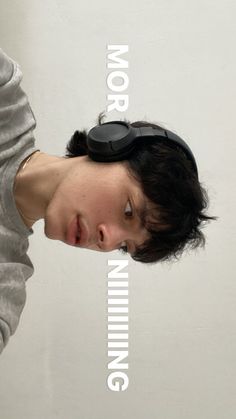 a young man with headphones on his ears is looking at the camera while standing in front of a white wall