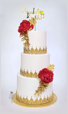 a three tiered wedding cake with red flowers on top and gold trimmings