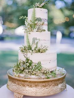 a white wedding cake with greenery on top and gold plated serving platter