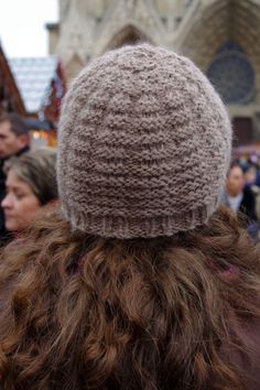 the back of a person's head wearing a knitted hat in front of a cathedral