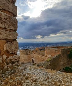 an old stone building sitting on top of a rocky hill next to a city under a cloudy sky