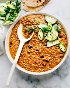 a bowl of soup with cucumbers, bread and pita chips on the side