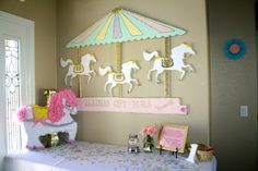 a pink and white table topped with a carousel ride next to a window covered in confetti