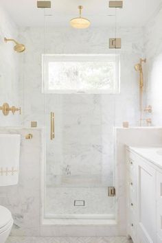 a white bathroom with gold fixtures and marble flooring, along with a walk in shower