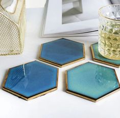 three blue hexagonal coasters next to a glass vase on a white table