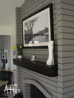 the fireplace is painted gray and has a white vase with yellow flowers on it next to a framed photograph