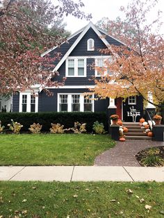 a black house with white trim and pumpkins on the front porch, in autumn