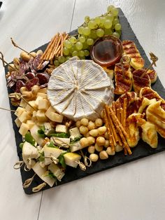 an assortment of cheeses, crackers and grapes on a slate platter