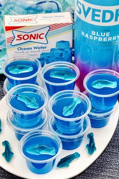 blue liquid in plastic cups on a plate next to a bottle of soda and some toothpaste