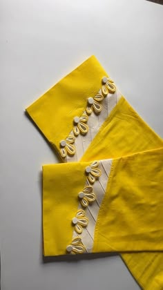 two pieces of yellow cloth with white thread on them, one is folded up and the other has buttons