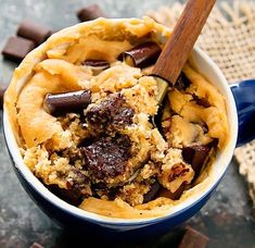 a blue bowl filled with dessert and chocolate chips on top of a table next to a wooden spoon