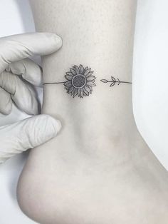 a sunflower tattoo on the ankle with an arrow in front of it that is attached to