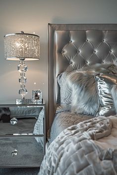 a bed with silver sheets and pillows next to a mirrored night stand in a bedroom