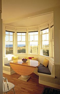 a room with three windows and a table in the corner next to two white chairs