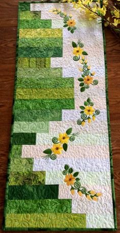 a quilted table runner with yellow flowers and green leaves on it's edge