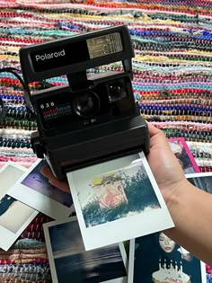 an old polaroid camera is being held by someone's hand over a pile of photos