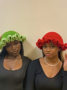 two women wearing matching hats standing next to each other in front of a white wall