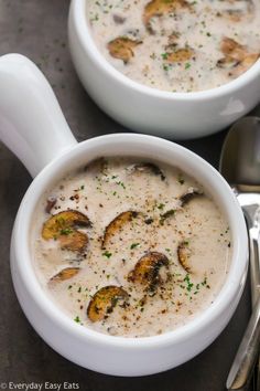 two white bowls filled with soup on top of a table next to silver spoons