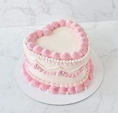 a heart shaped cake with pink and white icing on a plate next to a marble counter top