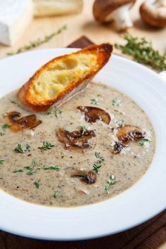 a white bowl filled with mushroom soup on top of a wooden table next to a piece of bread