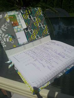 an open notebook sitting on top of a table next to a swimming pool with papers and pens