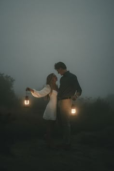 a man and woman standing in the fog holding two lanterns with their arms around each other