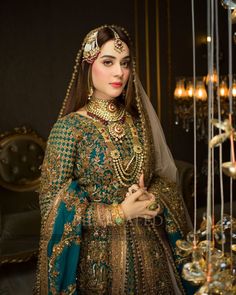 a woman in a green and gold bridal outfit standing next to chandelier