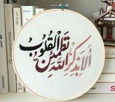 a cross stitch pattern with arabic writing on it and some books in the back ground